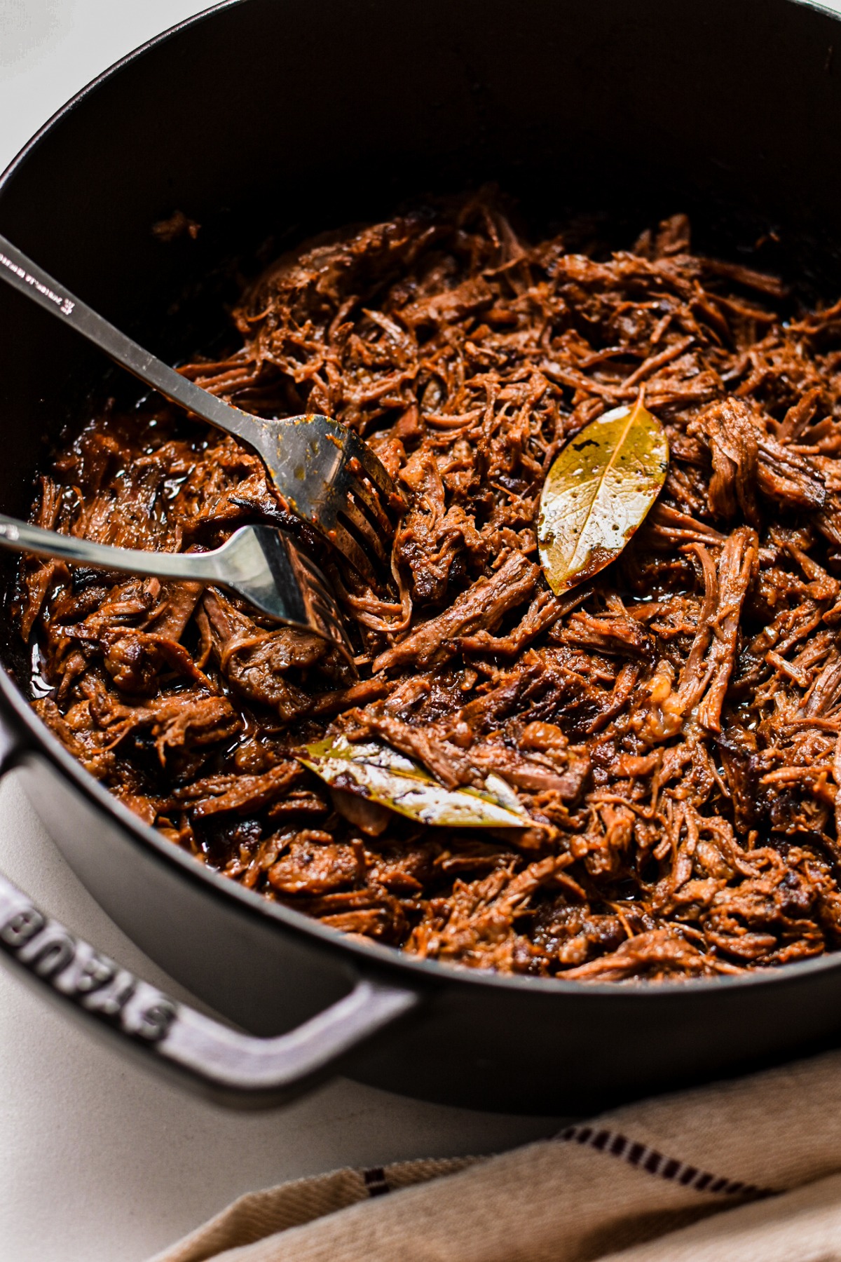 Shredded beef barbacoa in a cast iron pan with two forks.