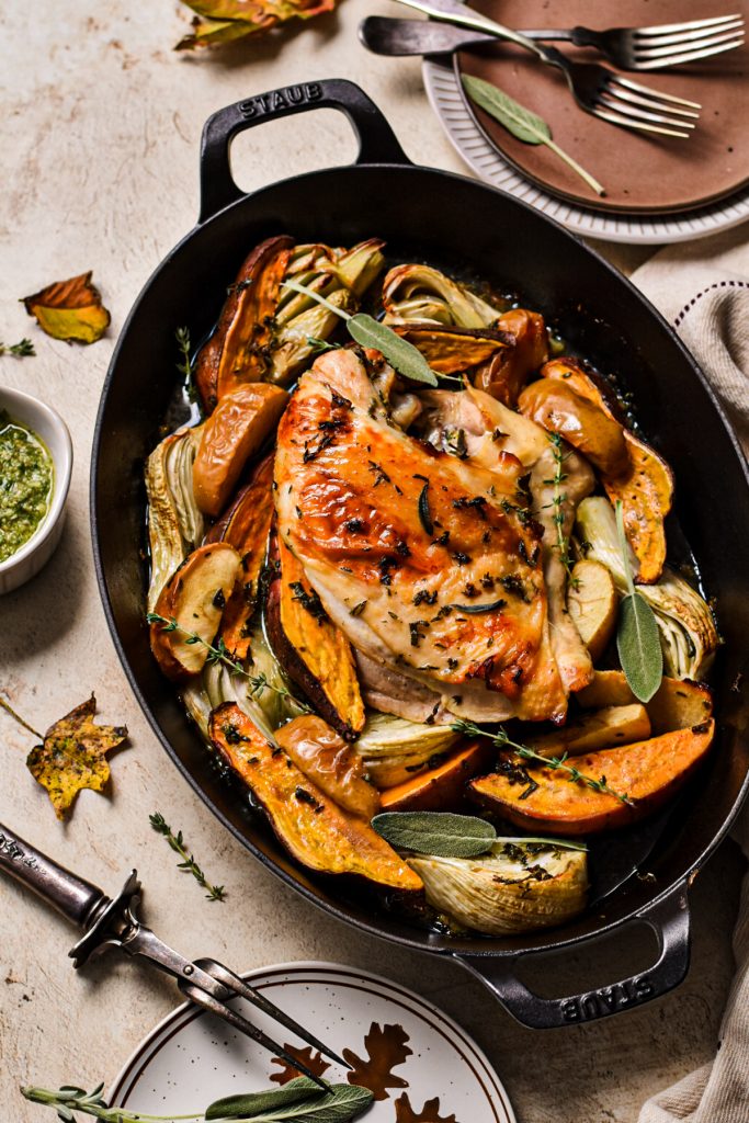 Turkey breast in a roasting pan with vegetables around it and fresh herbs on top.