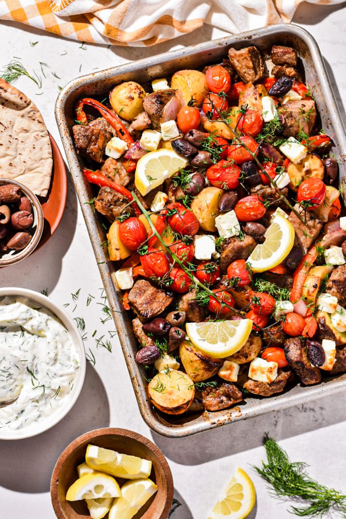 Overhead shot of sheet pan pork soulvaki on a sheet pan garnished with lemon wedges.