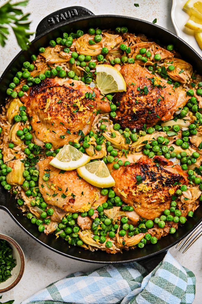 One pan lemon chicken and rice in a cast iron skillet with peas and artichokes.