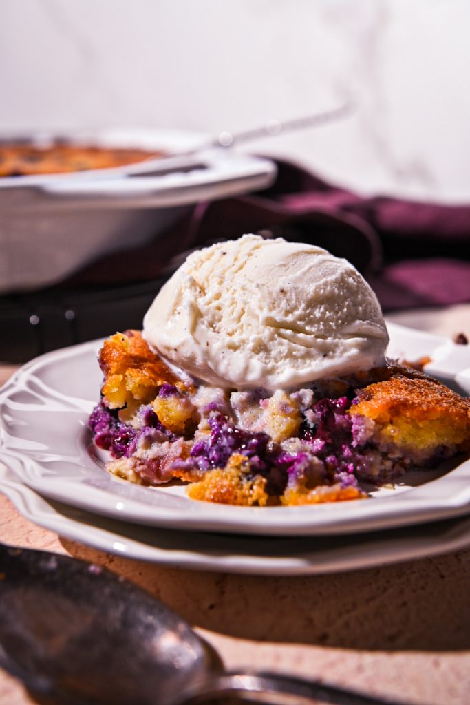Side view of a portion of blueberry rhubarb gratin with ice cream on top.