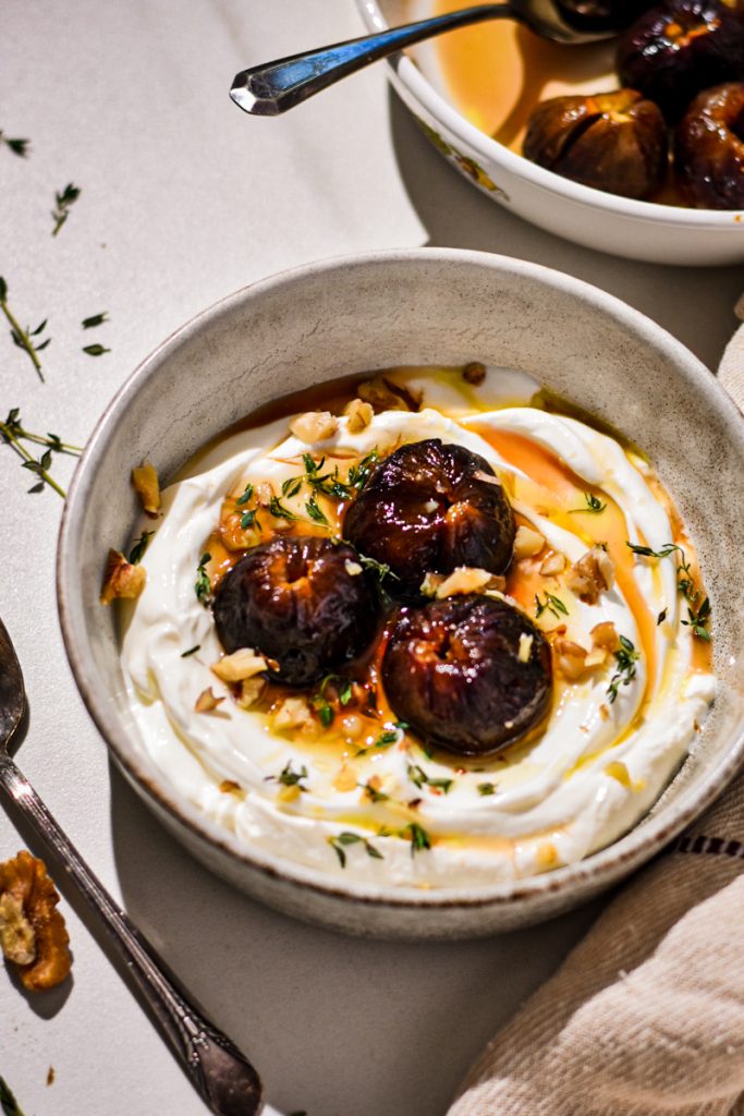 Roasted figs with yogurt in a bowl topped with walnuts and thyme.
